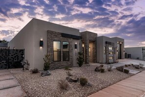 A modern two-story house with a stone facade, large windows, and a gravel driveway. - Pecan Valley Oasis | Private Backyard Paradise (Hurricane)
