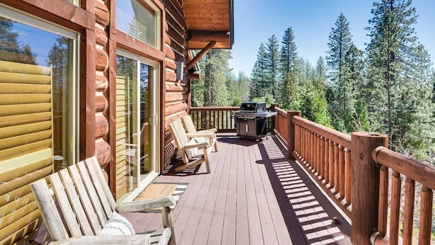 A wooden deck with chairs and a grill, overlooking a forest. - Cozy Log Cabin, Ping Pong, Firepit, Dog friendly! (Arnold)
