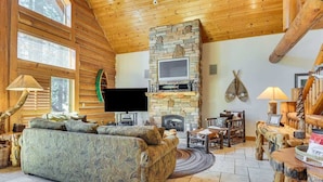 A log cabin interior with a stone fireplace, a television, a sofa, and rustic wooden furniture. - Cozy Log Cabin, Ping Pong, Firepit, Dog friendly! (Arnold)
