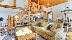 A spacious living area with a wooden staircase, a sofa, and a dining table. - Cozy Log Cabin, Ping Pong, Firepit, Dog friendly! (Arnold)