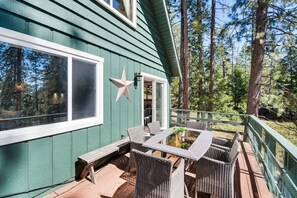 Eine Holzterrasse mit Korbmöbeln, einer Stern-Dekoration und einem Haus mit grünen Holzverkleidungen.