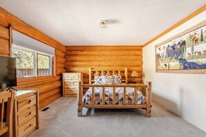 Ein Schlafzimmer in einer Blockhütte mit einem hölzernen Bett, einem Schreibtisch und einem Fenster.
