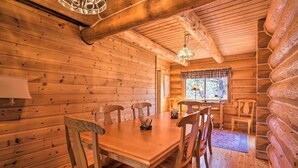 A wooden cabin interior with a dining table, chairs, a chandelier, and a window with curtains. - Log Home w/view, Ping Pong, Cornhole, Gas FirePit! (Bend)