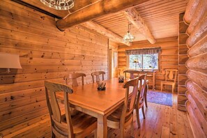 A wooden cabin interior with a dining table, chairs, a chandelier, and a window with curtains. - Log Home w/view, Ping Pong, Cornhole, Gas FirePit! (Bend)