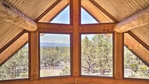 A room with a sloped wooden ceiling and large windows offering a view of a forested area. - Log Home w/view, Ping Pong, Cornhole, Gas FirePit! (Bend)
