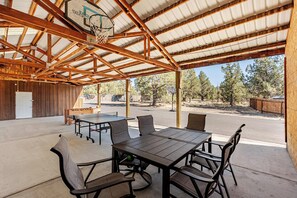 An outdoor covered patio with a basketball hoop, tables, and chairs. - Log Home w/view, Ping Pong, Cornhole, Gas FirePit! (Bend)