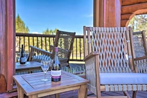Eine Holzterrasse mit Korbstühlen, einem Tisch, einer Weinflasche und einem Glas.