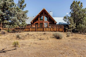 A wooden gazebo with a triangular roof, surrounded by a wooden fence, in a dry grass field with trees in the background. - Log Home w/view, Ping Pong, Cornhole, Gas FirePit! (Bend)