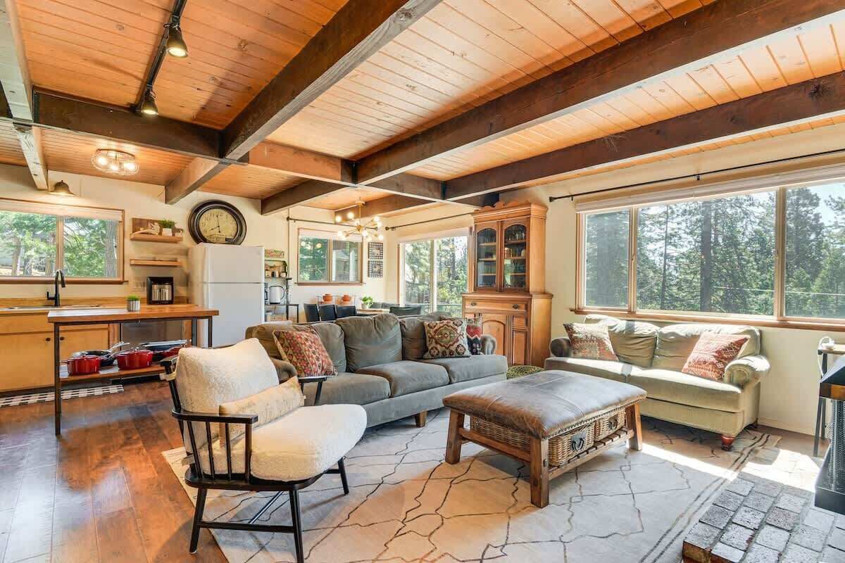 A spacious living area with a wooden ceiling, large windows, a sofa, a chair, and a fireplace.