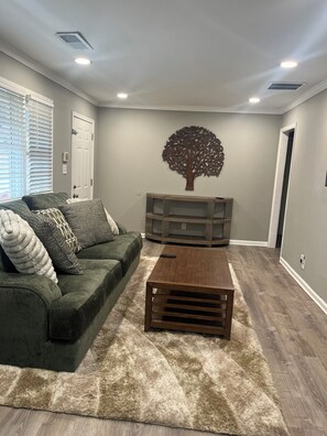 Ein Wohnzimmer mit einem grünen Sofa, einem Holztisch und einer Wanddekoration mit Bäumen.