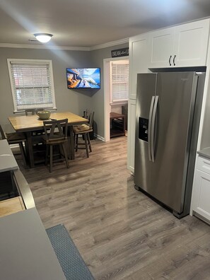 Eine moderne Küche mit einem Edelstahl-Kühlschrank, einem Holzesstisch und einem flachbildfernseher an der Wand.