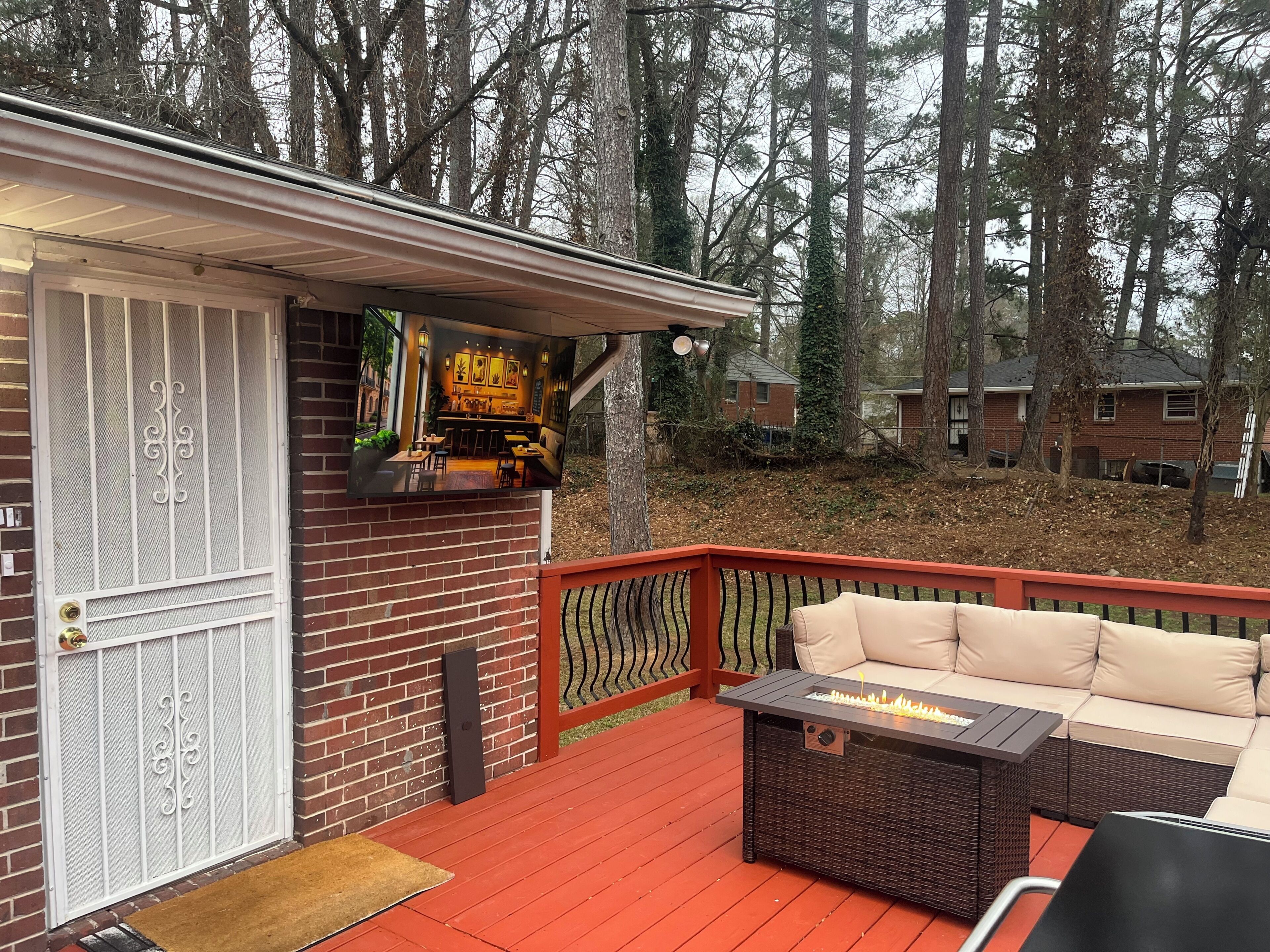 A deck with a red railing, a wicker sofa, and a fire feature.