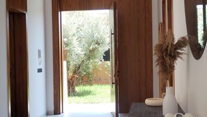 Un hall d’entrée spacieux avec un parquet en bois foncé, un grand miroir sur le côté droit et une vue sur un jardin, visible à travers une porte en bois.