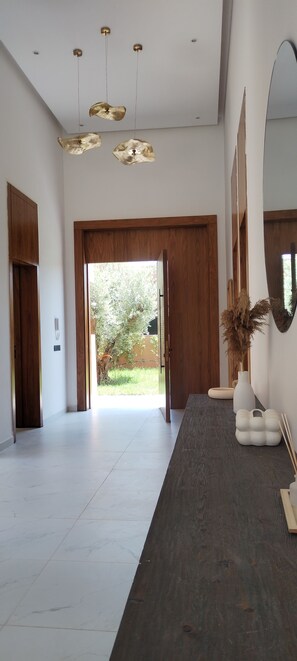 A spacious hallway with a dark wooden floor, a large mirror on the right, and a view of a garden through a wooden door. - Villa de Luxe avec Piscine Privée - Une Oasis d'Exception à Marrakech ". (Marrakesh)