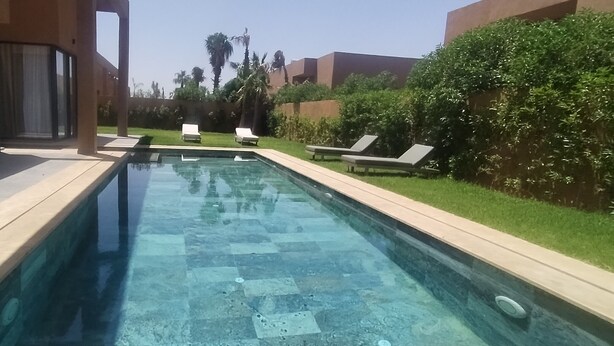 Une piscine avec des chaises longues, une entrée avec une porte vitrée et une pelouse bien entretenue.