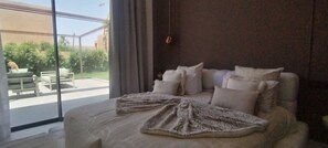 A bedroom with a large bed, a view of the outdoors, and a window with curtains. - Villa de Luxe avec Piscine Privée - Une Oasis d'Exception à Marrakech ". (Marrakesh)