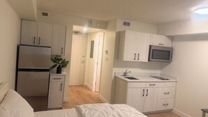 Ett kompakt hotellrum med en säng, ett litet kök och en dörr som leder till ett annat rum.