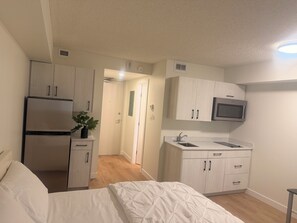 Una habitación de hotel compacta con cama, kitchenette y una puerta que conduce a otra habitación.
