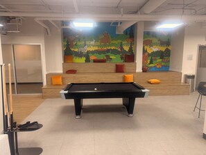 A pool table in a room with a mural of animals and a staircase with colorful cushions.