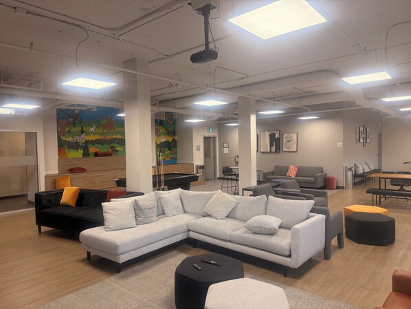A modern lounge area with a sectional sofa, a pool table, and a bar area.