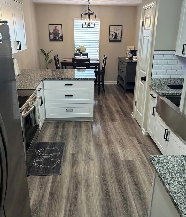 A kitchen with a central island, white cabinetry, granite countertops, and a wooden floor.
