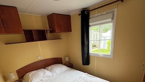 Een slaapkamer met een groot bed, een nachtkastje, een lamp, een raam met gordijnen en inbouw houten kasten.