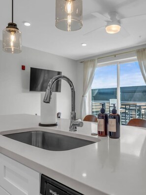 Una cocina moderna con una isla grande, pileta de acero inoxidable e iluminación colgante.
