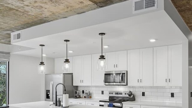A modern kitchen with white cabinets, a central island, bar stools, and pendant lighting. - Summit Hill Stay | King Suite | Free Parking (Knoxville)