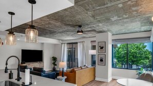 A modern kitchen with a large island, a dining area with a round table, a sofa, and a TV. - Summit Hill Stay | King Suite | Free Parking (Knoxville)