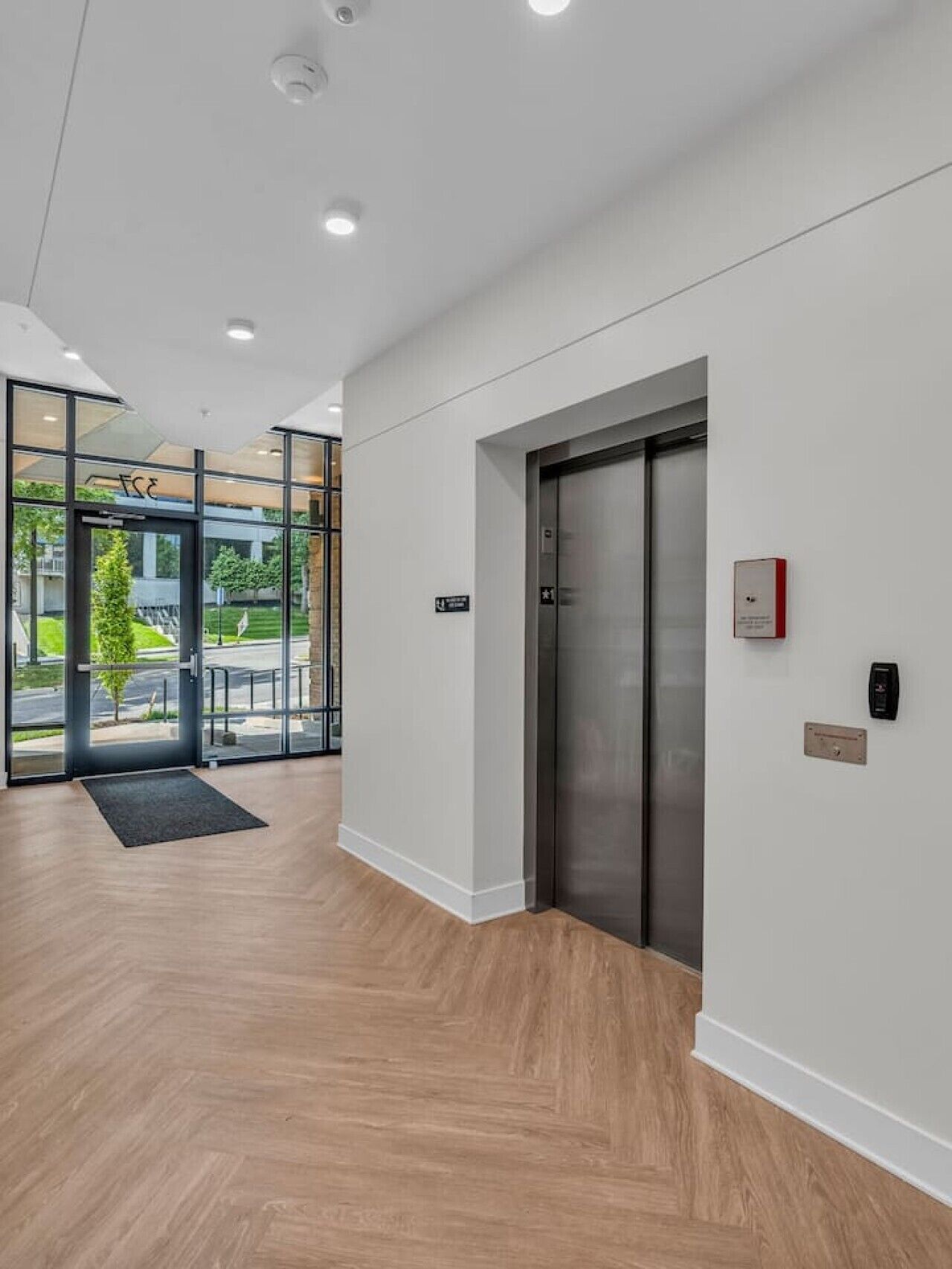A modern interior with a wooden floor, a glass door entrance, and a metallic elevator.
