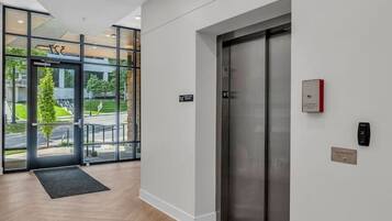 A modern interior with a wooden floor, a glass door entrance, and a metallic elevator.