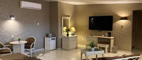 Une chambre d’hôtel équipée d’un lit, d’une télévision, d’un bureau, d’une chaise, d’une petite table, d’une lampe et d’un appareil de climatisation.