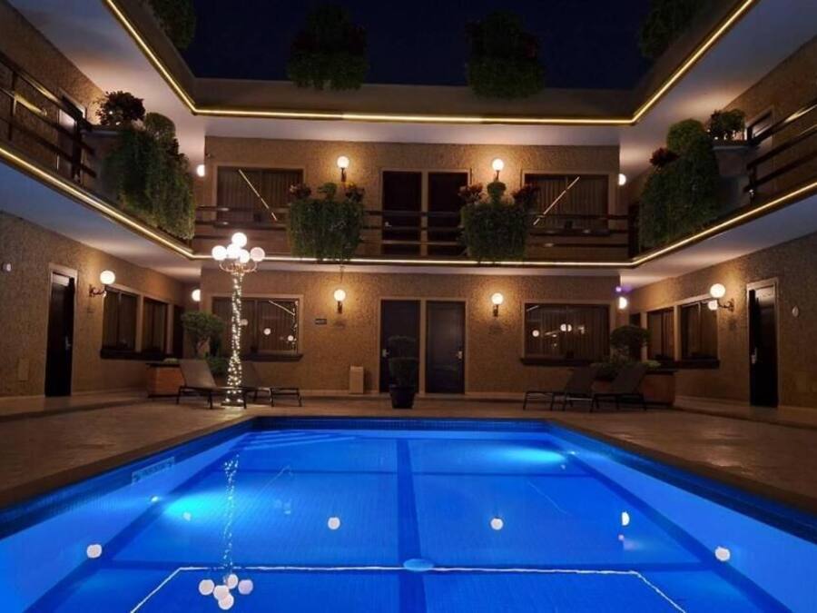 Zona de piscina con una fuente, rodeada por un edificio con balcones y plantas.