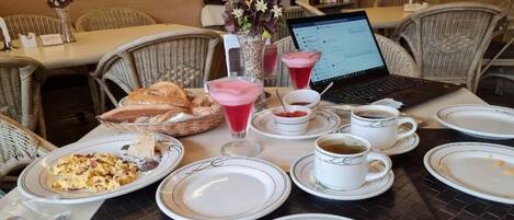 Una mesa de comedor preparada con platos, vasos, una computadora portátil y una cesta de pan.