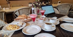 Una mesa de comedor preparada con platos, vasos, una computadora portátil y una cesta de pan.