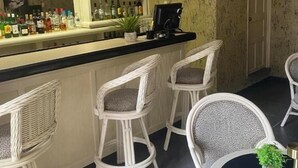 A bar area with wicker chairs, a counter with bottles, and a television mounted on the wall. - Hotel Casa Layun (Cordoba)