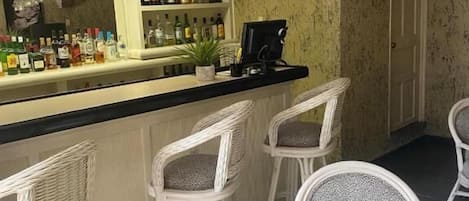 A bar area with wicker chairs, a counter with bottles, and a television mounted on the wall.