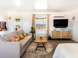 A modern living room with a sofa, a coffee table, a TV, and a view of the desert.