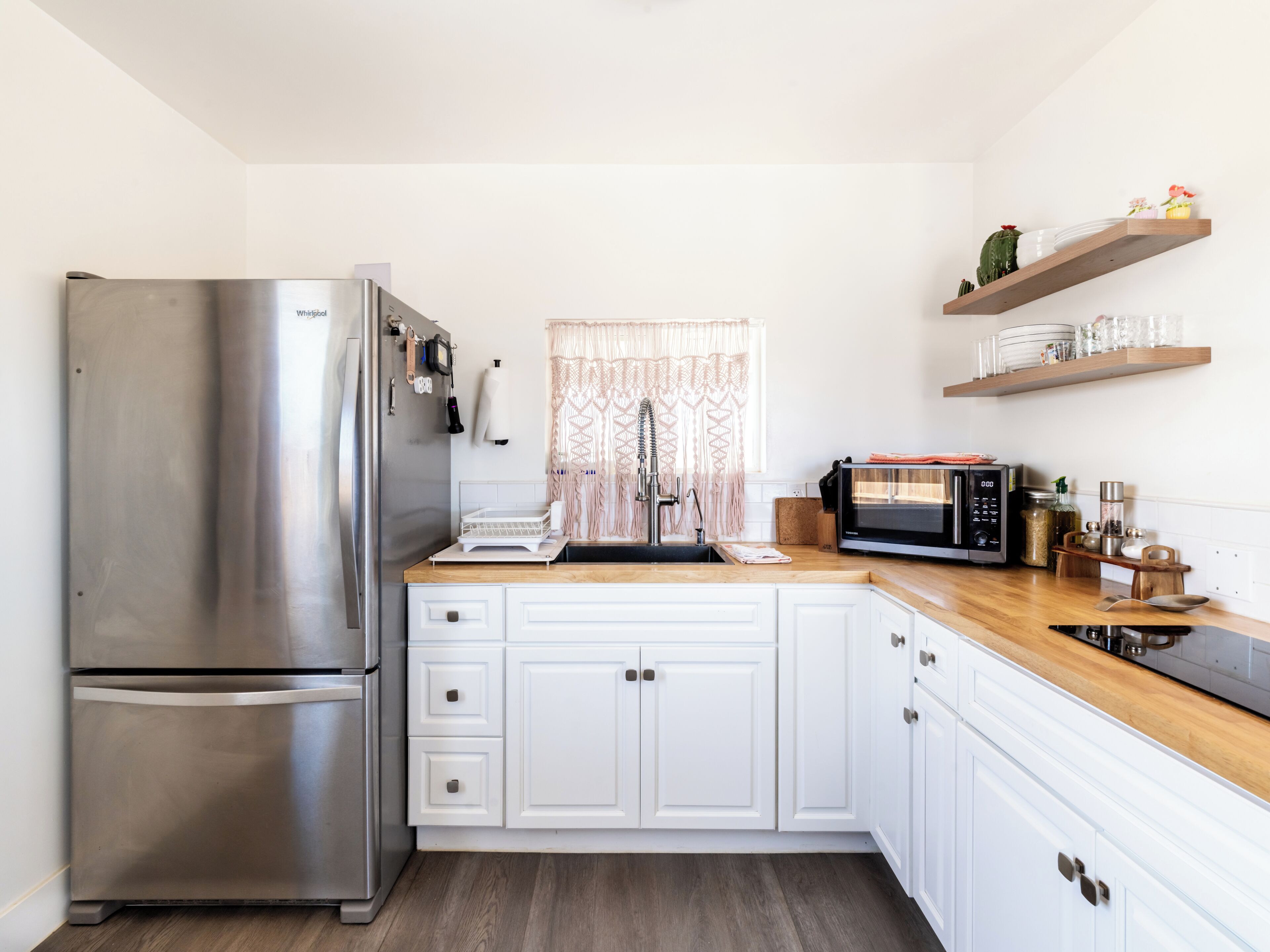 A kitchen with white cabinets, a stainless steel refrigerator, a microwave, and wooden countertops.