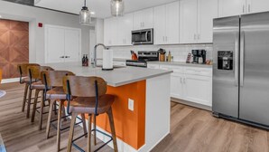 Una cucina moderna con mobili bianchi, un frigorifero in acciaio inossidabile, un microonde integrato e una zona bar con sgabelli.