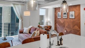 Een moderne keuken met een centraal eiland, een zithoek met een bank en tafel, en stadszicht door grote ramen.