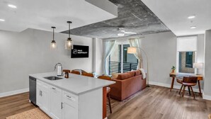 Een moderne keuken met een centraal eiland, een zithoek met tafel en stoelen, een bank en uitzicht op een balkon.