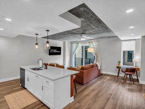 A modern kitchen with a central island, a dining area with a table and chairs, a sofa, and a view of a balcony. - Lone Tree Escape | King Bed | Stylish DT Stay (Knoxville)
