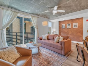A modern living room with a sofa, coffee table, and chairs, a balcony with a railing, and a ceiling fan. - Lone Tree Escape | King Bed | Stylish DT Stay (Knoxville)