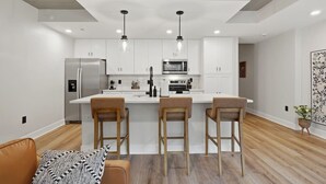 Una cocina moderna con armarios blancos, una isla central con taburetes de bar, un refrigerador de acero inoxidable y un microondas.