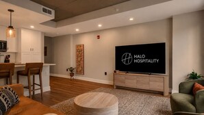 Una sala moderna con un televisor de pantalla plana grande, un taburete redondo de madera y una zona de bar con taburetes.