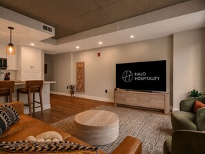 Ein modernes Wohnzimmer mit einem großen Flachbildfernseher, einem runden Holzhocker und einer Bar mit Sitzgelegenheiten.