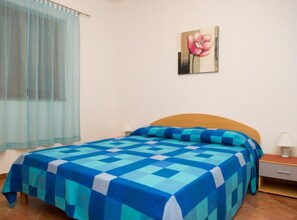 A bedroom with a bed, a nightstand, a lamp, a window with sheer curtains, and a wall-mounted painting. - One Bedroom Apartment with Terrace (Vodice)
