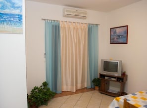 A room with a television on a wooden stand, a potted plant, and a painting on the wall. - One Bedroom Apartment with Terrace (Vodice)
