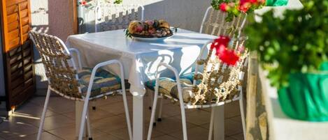 An outdoor patio with a table and chairs, a potted plant, and a window with a view.